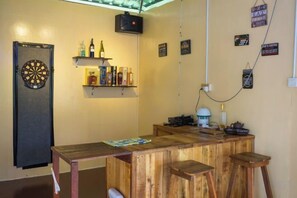Angolo bar con bersaglio da freccette, scaffali con bottiglie e bancone in legno.