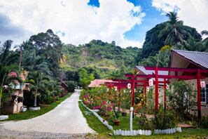 A pathway leading to a building with a red roof, surrounded by lush greenery and a hill in the background. - Timba Garden Semporna Free Town / Jetty Transport (Semporna)