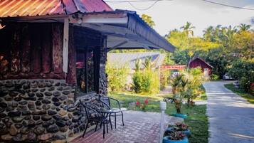 A stone building with a red roof, a covered patio with chairs, and a pathway leading to a red-roofed structure.