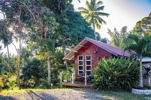 Une cabane en bois dotée d’une véranda, entourée d’une végétation tropicale.