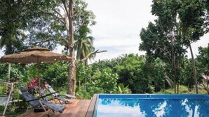 A pool area with lounge chairs and a thatched umbrella. - Timba Garden Semporna Free Town / Jetty Transport (Semporna)