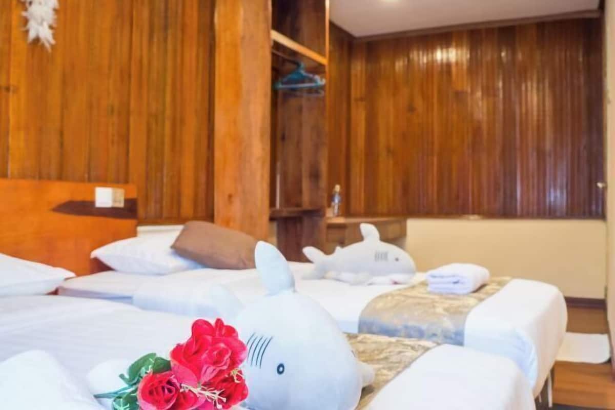 A hotel room with wooden paneling, a bed with white linens, a plush shark decoration, and a bouquet of red flowers.