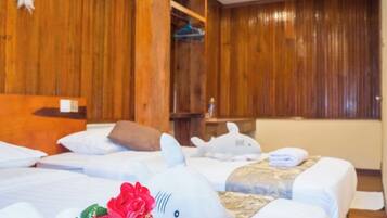 A hotel room with wooden paneling, a bed with white linens, a plush shark decoration, and a bouquet of red flowers.