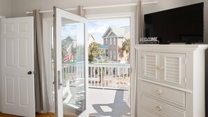 A room with a sliding glass door leading to a balcony, a television on a cabinet, and a welcome sign. - Charming Ocean View Retreat- Steps to the Beach and Pool- Resort-Style Amenities (Saint Helena Island)