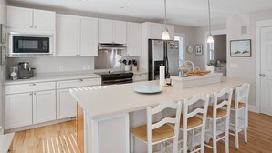 A modern kitchen with white cabinetry, a central island with bar stools, stainless steel appliances, and pendant lighting. - Charming Ocean View Retreat- Steps to the Beach and Pool- Resort-Style Amenities (Saint Helena Island)