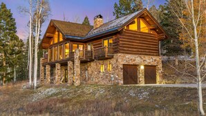 A log cabin with a stone foundation, large windows, and a balcony.