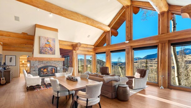 A spacious living room with a fireplace, large windows, and a view of the mountains.