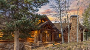 A log cabin with a stone chimney, wooden porch, and a stone wall.