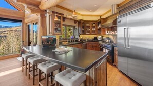 A modern kitchen with a large island, stainless steel appliances, wooden cabinetry, and a view of the mountains.