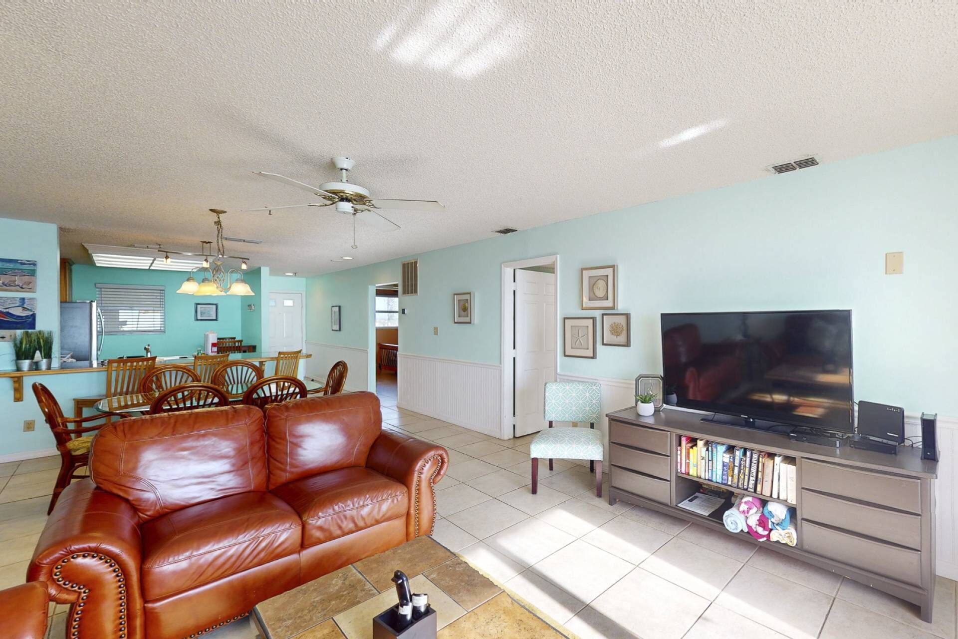 A living room with a brown leather sofa, a television, and a bookshelf.