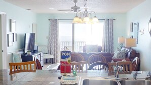 A kitchen with a dining area, a ceiling fan, and a large window with curtains.