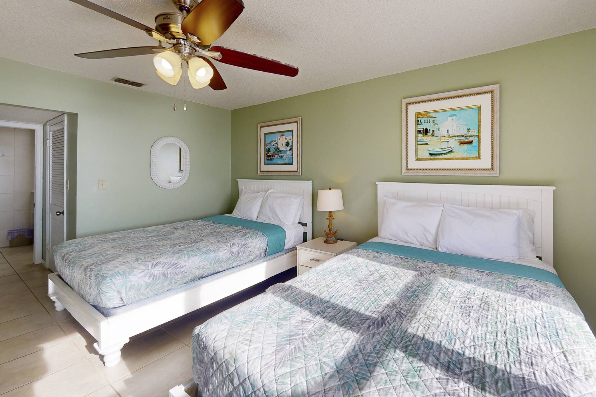 A hotel room with two single beds, a ceiling fan, and two framed pictures on the wall.