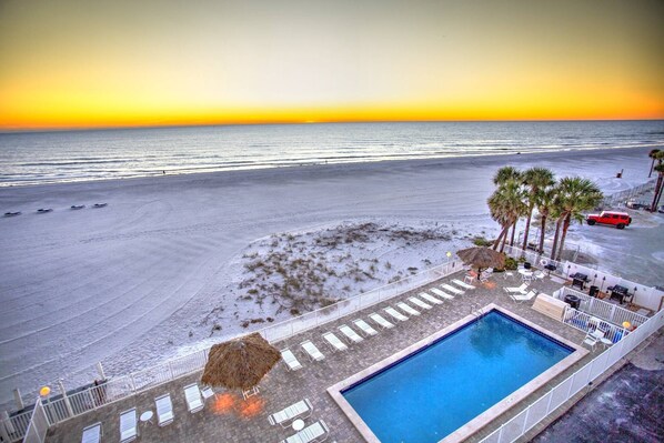 Zona de piscina con sillones de descanso y una piscina, con vista a una playa y un atardecer.