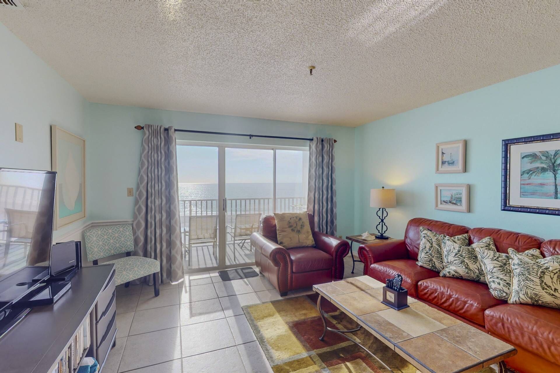 A living room with a TV, a sofa, a coffee table, and a balcony with a view of the sea.