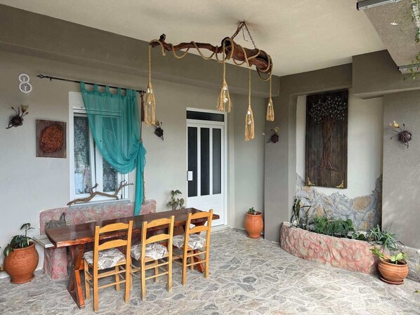 A dining area with a stone floor, wooden table and chairs, a hanging light fixture, and potted plants.