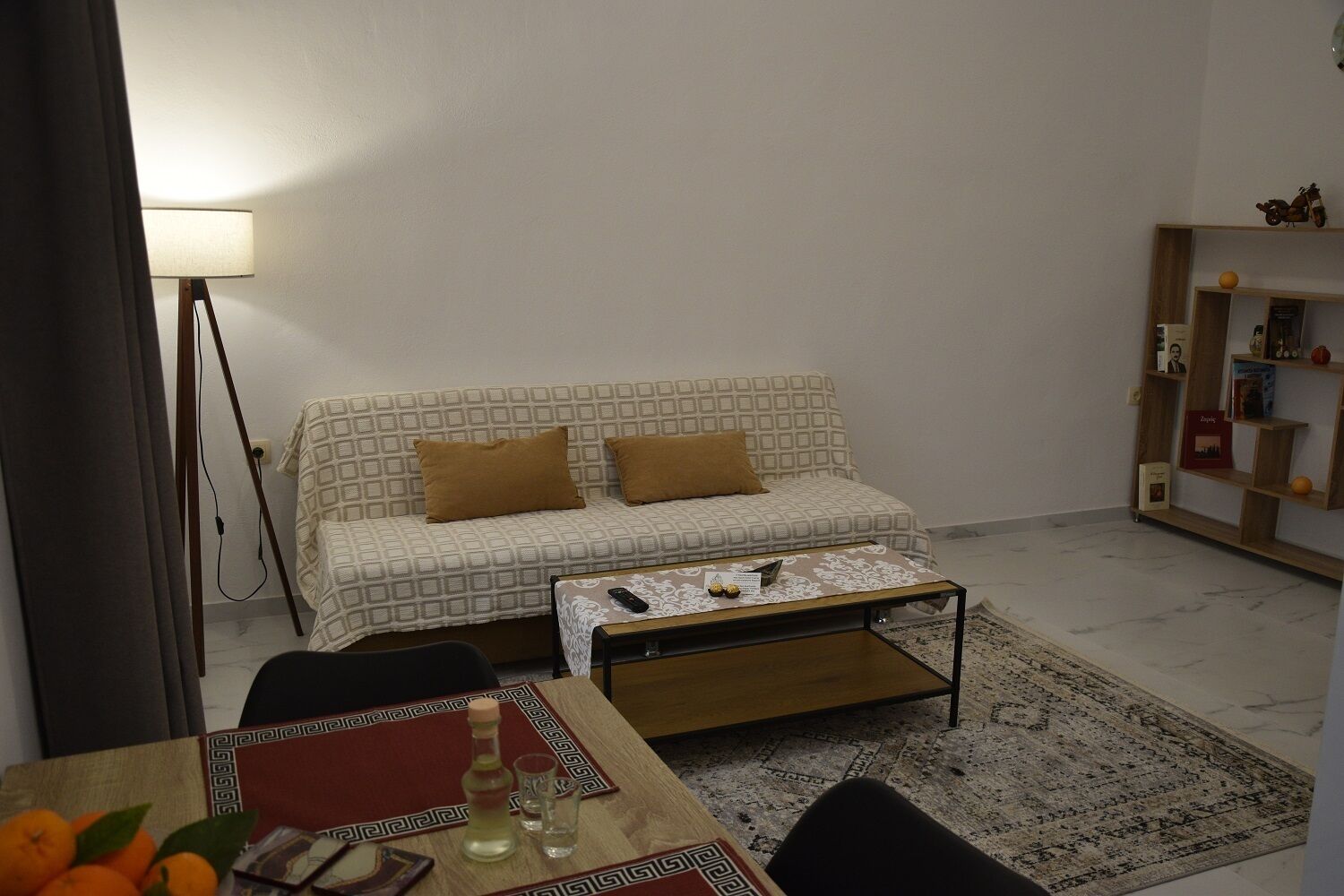 Ein Wohnzimmer mit einem gemusterten Sofa, einem Couchtisch, einer Lampe und einem Bücherregal.