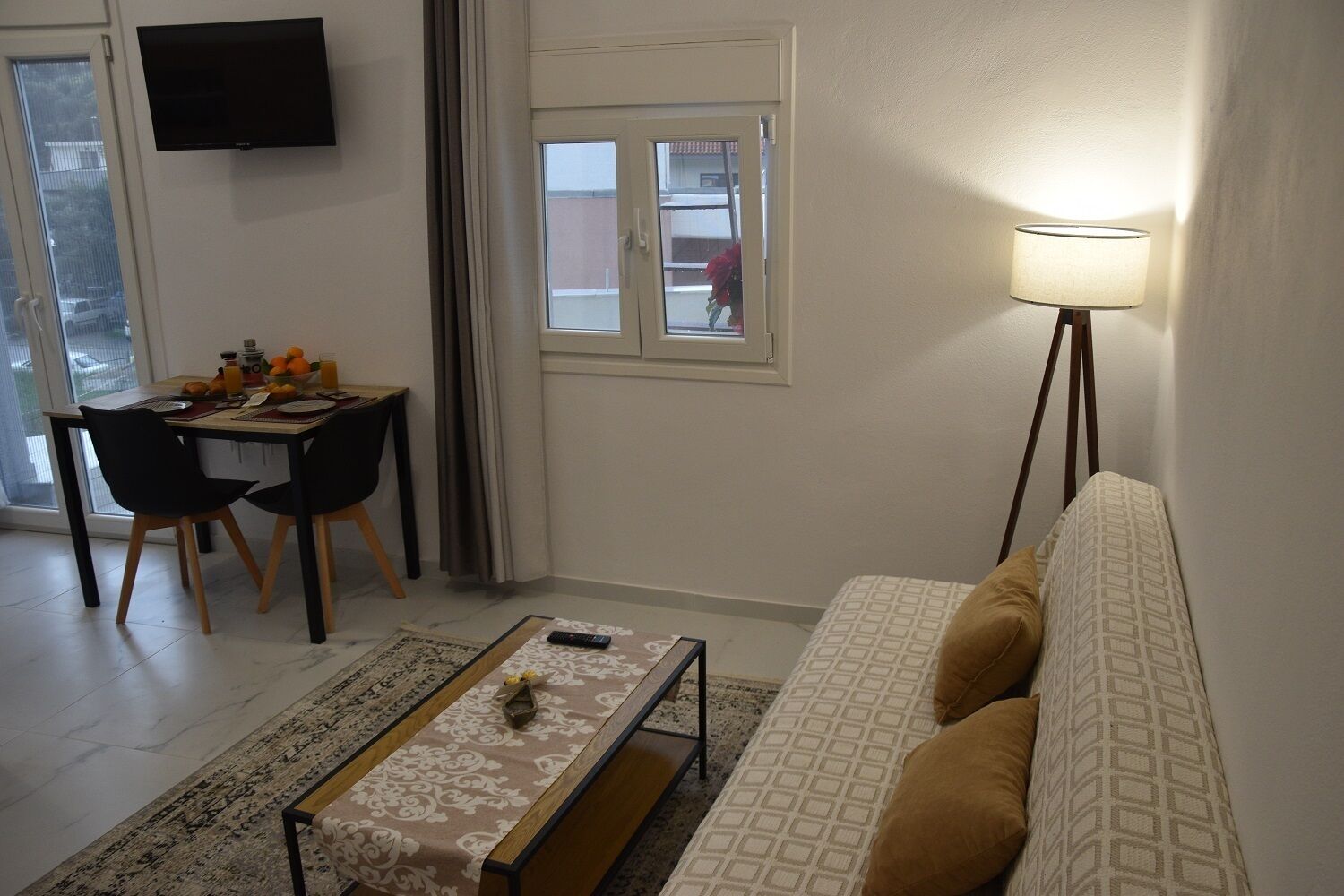 A living room with a sofa, a coffee table, a TV, and a dining area with chairs and a table.