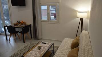 A living room with a sofa, a coffee table, a TV, and a dining area with chairs and a table.