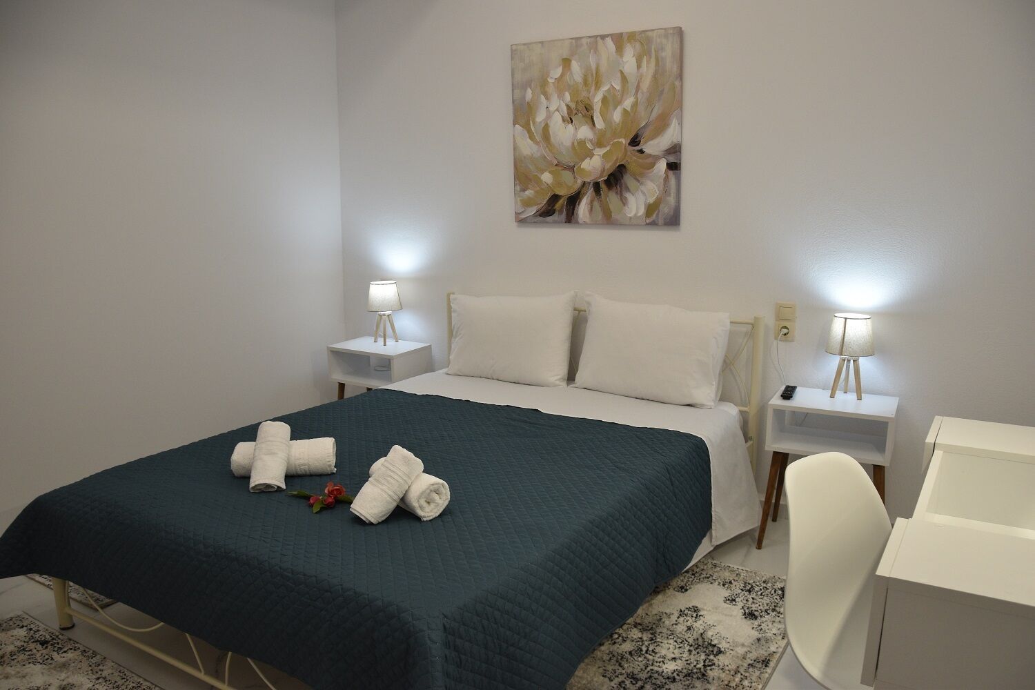 A hotel room with a bed, two bedside tables with lamps, a desk, and a painting on the wall.
