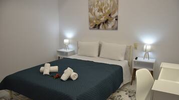 A hotel room with a bed, two bedside tables with lamps, a desk, and a painting on the wall.