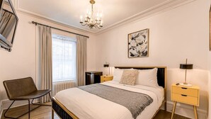 A modern bedroom with a large bed, a chair, bedside tables, a chandelier, and a window with curtains. - Standard Room #3 (Québec)