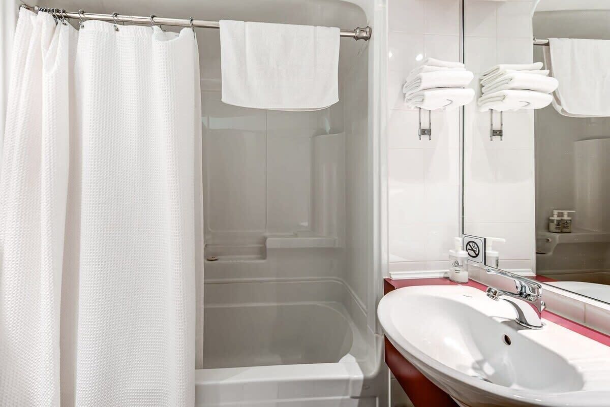 Une salle de bain avec un rideau de douche, une baignoire, un lavabo avec un miroir et des serviettes suspendues sur un porte-serviettes.