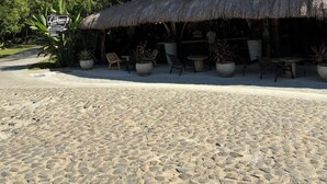 Ein Gebäude direkt am Strand mit einem Reetdach, Außenplätzen und einem Schild, das auf ein Burger-Café hinweist.