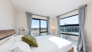 A bedroom with a bed, a nightstand, a lamp, and a view of the outside. - StarRain Tekapo (Lake Tekapo)