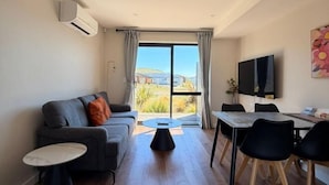 A modern living room with a sofa, a coffee table, a dining table with chairs, a flat-screen TV, and a large window with curtains. - StarRain Tekapo (Lake Tekapo)