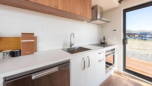 A modern kitchen with white cabinets, stainless steel appliances, and a large window offering a view of the outdoors. - StarRain Tekapo (Lake Tekapo)