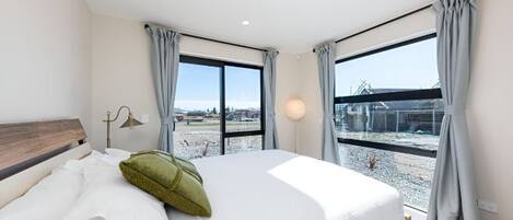 A modern hotel room with a large bed, a view of a cityscape, and a window with curtains.