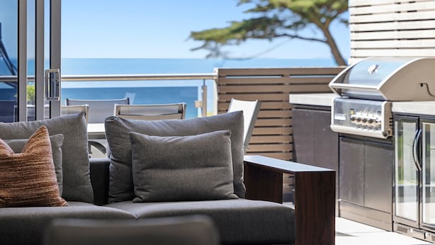 Un espace extérieur moderne, aménagé avec des sièges, un barbecue et une vue sur l’océan.