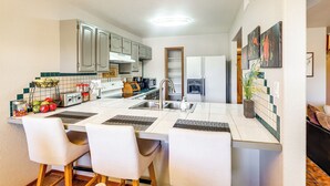 Una cucina moderna con mobili bianchi, un'isola centrale con sedute e forno a incasso, oltre a un forno a microonde.