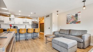 A modern kitchen with white cabinets, a dining area with a long table and four chairs, a grey sofa, and a small round table. - Walk to Dtwn: Winter Park Studio w/ Hot Tub Access (Winter Park)