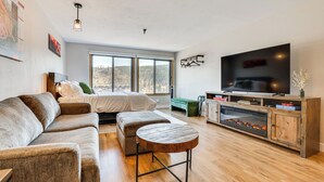 A modern living room with a sofa, ottoman, and a television on a wooden cabinet. - Walk to Dtwn: Winter Park Studio w/ Hot Tub Access (Winter Park)