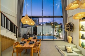 Un espace repas moderne avec une grande table, des chaises et une vue sur une piscine, grâce à de larges fenêtres.