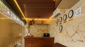 Un espace d’accueil comprenant un canapé, un comptoir de réception en bois, une horloge murale et une grande fenêtre.