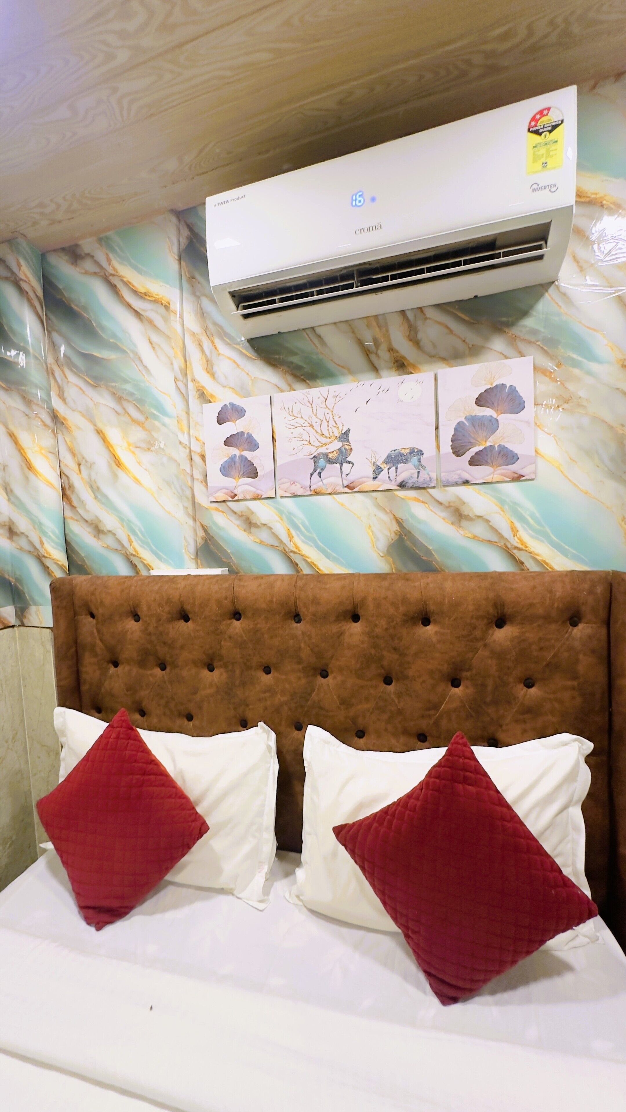 A hotel room with a marble-patterned wall, a brown tufted headboard, and a bed with white and red pillows.