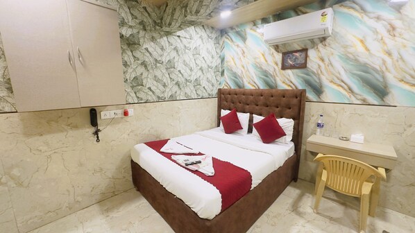 A hotel room with a bed, a desk, a chair, an air conditioner, and a wall with a leaf pattern. - Hotel Newyork by Stayzy Rooms (Mumbai)