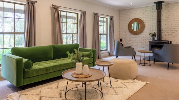A living room with a green sofa, two round tables, a beige ottoman, and a fireplace. - Furche Barossa Vineyard & Fireplace  (Stone Well)