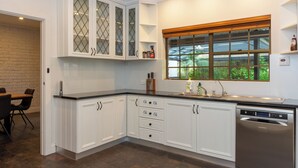 A modern kitchen with white cabinetry, a built-in dishwasher, and a window with a view of greenery. - Furche Barossa Vineyard & Fireplace  (Stone Well)
