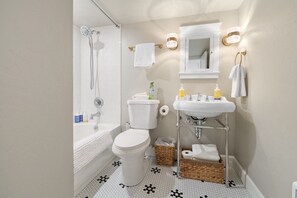 Ett badrum med en vit toalett, ett badkar, ett handfat och en dusch. Handdukar och hygienartiklar finns på hyllan.