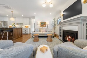 A modern living room with a fireplace, a sofa, two side tables, and a TV mounted on the wall. - Charming South Hill Craftsman Retreat near downtown—4BR, Smart TVs & Courtyard (Spokane)