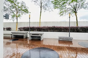 Un espacio exterior con terraza de madera, mobiliario y un muro bajo con plantas.