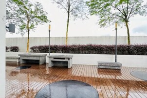 Un espacio exterior con terraza de madera, mobiliario y un muro bajo con plantas.