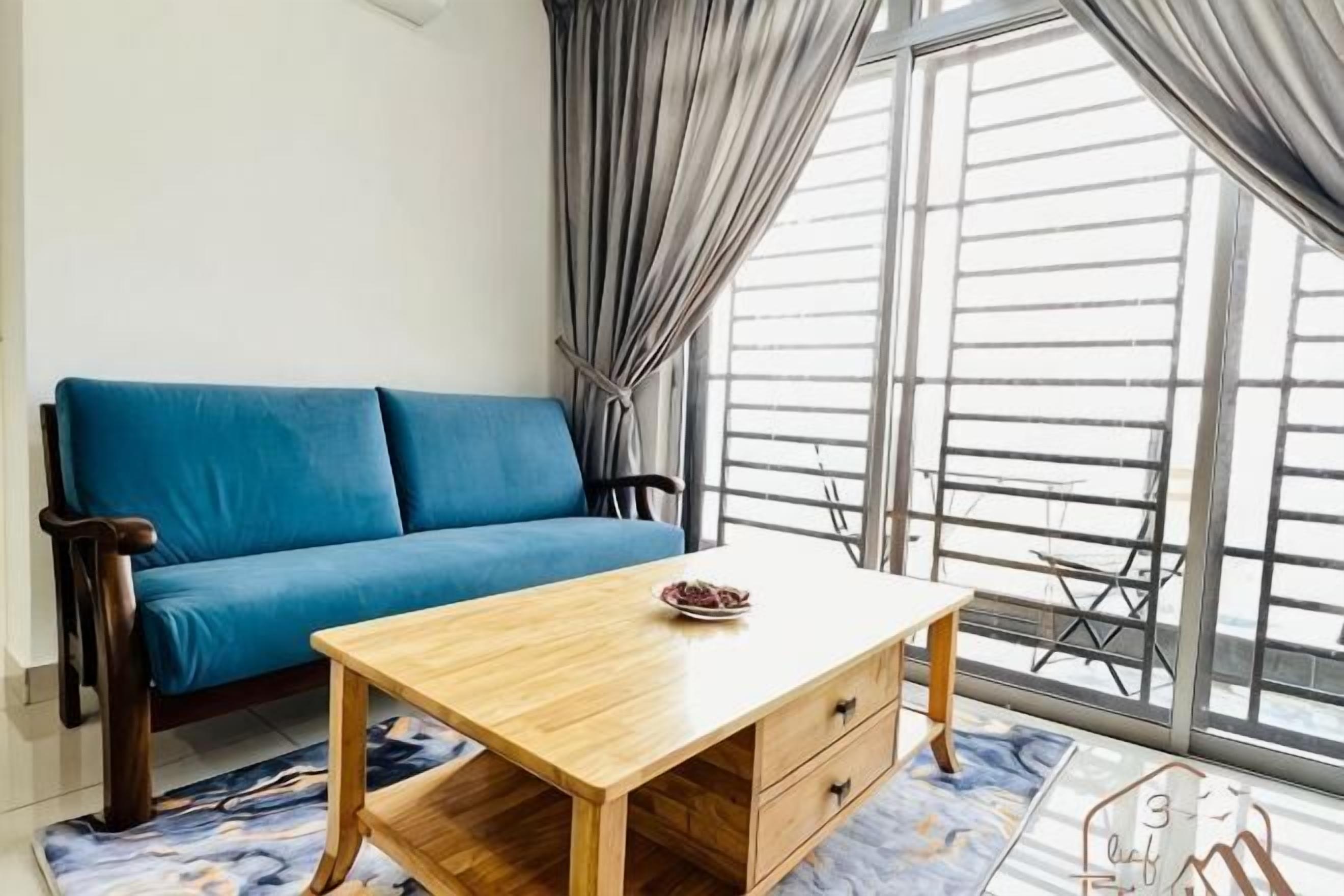 A room with a blue sofa, a wooden table with a bowl, and large windows with curtains.