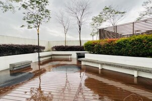 Un espacio al aire libre con una terraza de madera húmeda, bancos de asiento y una fuente de agua circular.