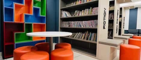 A library with colorful shelving units, a round table, and orange seating.