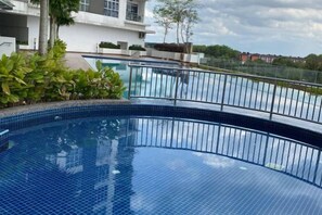 Una piscina con borde de azulejos, rodeada de una barandilla metálica, y una vista de una zona residencial al fondo.