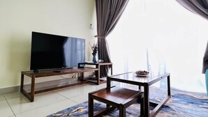 A room with a TV on a wooden stand, a small table, and a view of a building through large windows. - KULAI IOI Mall D'Putra Near JPO Senai Airport (Kulai)
